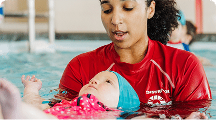 An instructor gently holds a baby learning to float on their back during a swim lesson.