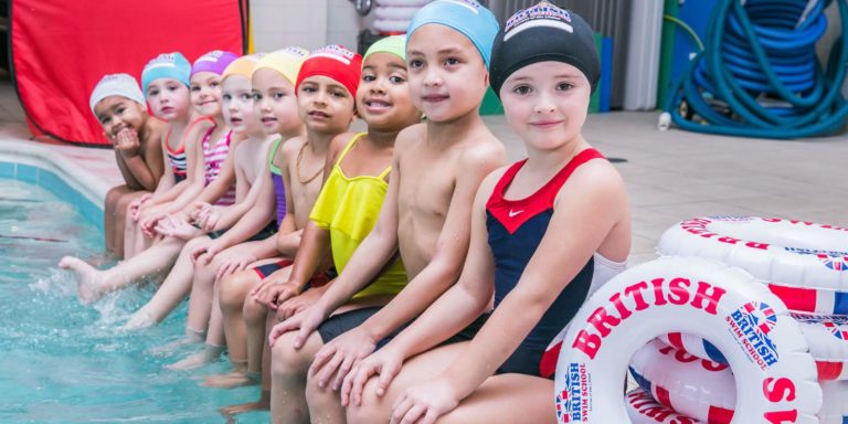 Children sitting on edge of pool smiling and ready for swim lessons
