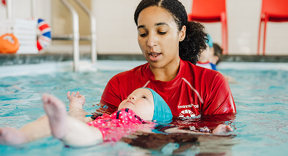 An instructor gently holds a baby on its back during a swimming lesson in a pool