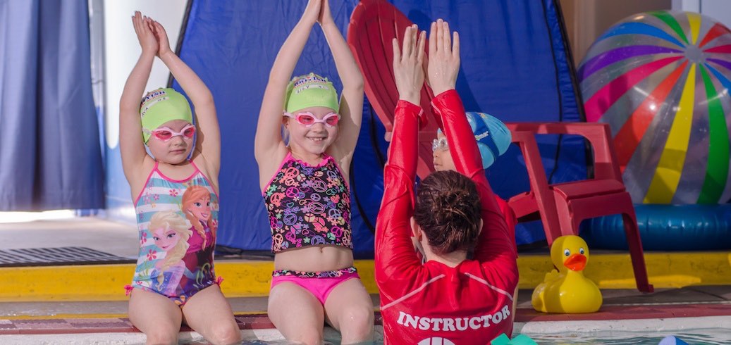 Two young girls and their instructor practice arm positions during a swim lesson. TITLE: