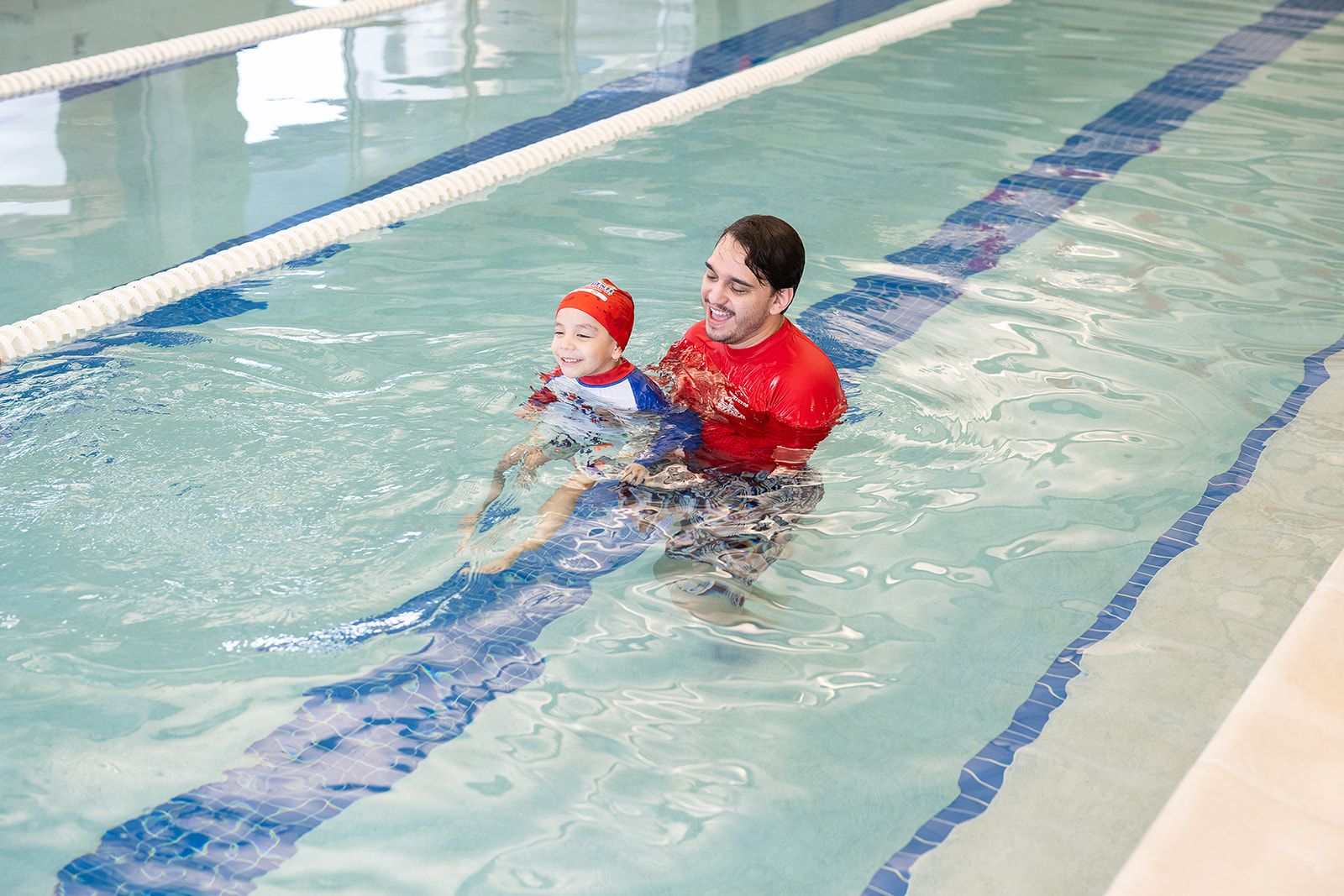 A young child learning to swim with the support of a friendly instructor during a British Swim School lesson in a West Seattle indoor pool.