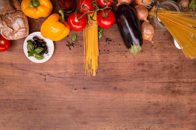 Fresh pasta, vegetables, bread, and olives are beautifully arranged on a rustic wooden surface.