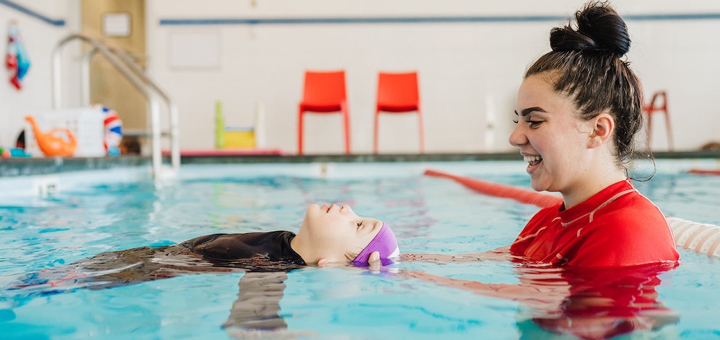 A smiling instructor helps a child float on their back during a swimming lesson.