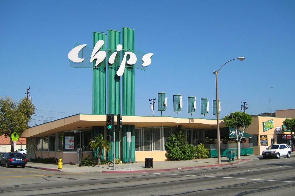The historic Chips Restaurant in Hawthorne, California, a landmark known for its mid-century Googie architecture and towering green pylon sign, stands under a clear blue sky at a bustling street corner. British Swim School offers year-round, indoor swim lessons for the South Bay community and surrounding Hawthorne, Inglewood, Lawndale, and Gardena neighborhoods.