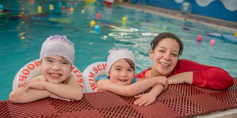 Two children with an instructor in the pool smiling