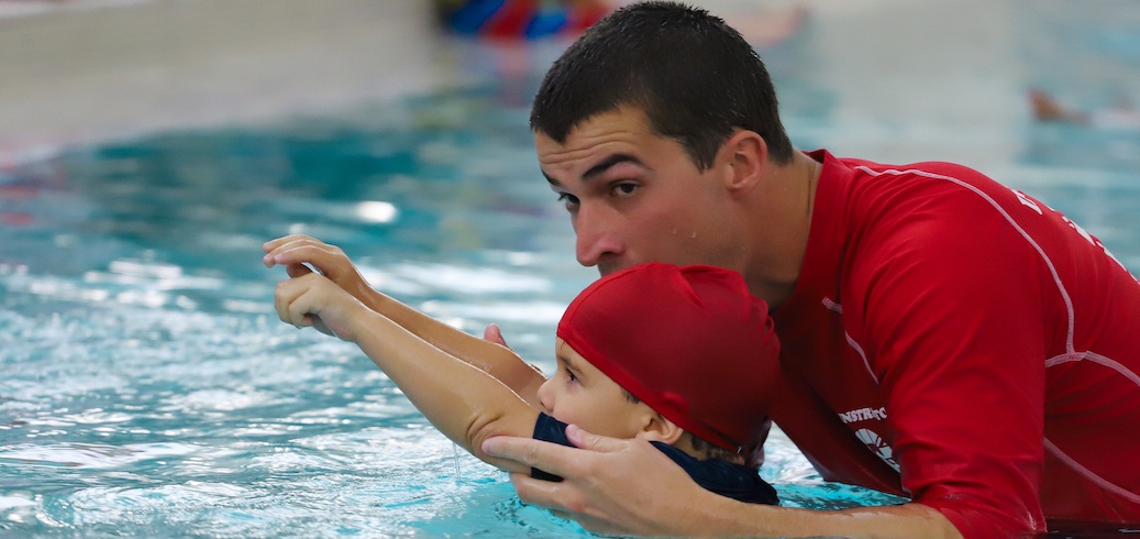 A swimming instructor teaches a young child to extend their arms in a pool.