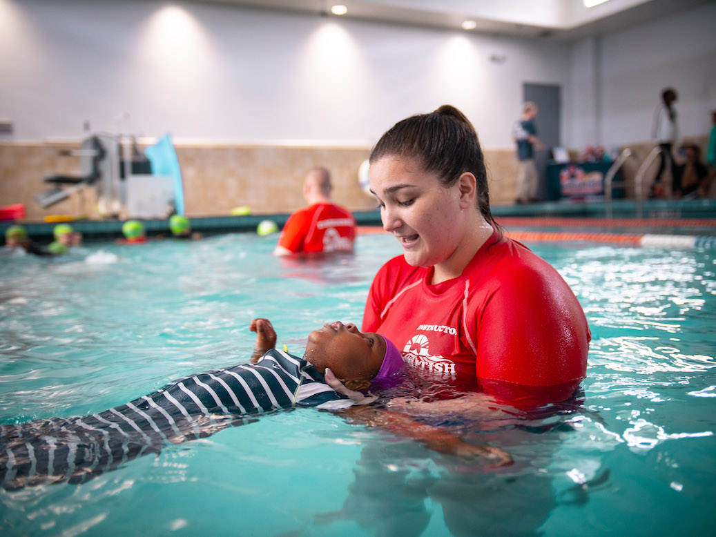 A swimming instructor gently helps a young child float on their back during a lesson.