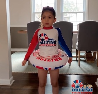 Young girl wearing a British Swim School rash guard and swim ring